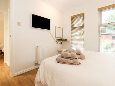 A bedroom with a bed and folded towels on it a wall-mounted television a radiator and windows with blinds at 10 Thirlmere White Cross Bay near Troutbeck Bridge
