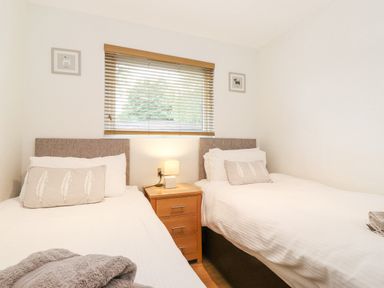A bedroom with two single beds a wooden nightstand with a lamp and window blinds at 10 Thirlmere White Cross Bay near Troutbeck Bridge