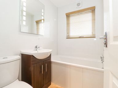 A bathroom with a toilet, a sink with wooden cabinet, a bathtub, a mirror, and a window with blinds at 10 Thirlmere White Cross Bay near Troutbeck Bridge