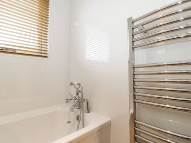 A bathroom with a bathtub a chrome faucet a handheld shower head a window with blinds and a wall-mounted chrome towel warmer at 10 Thirlmere White Cross Bay near Troutbeck Bridge