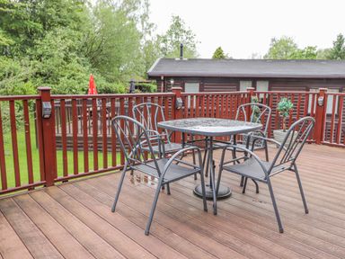 An outdoor deck with a metal table and four chairs next to a wooden railing at 10 Thirlmere White Cross Bay near Troutbeck Bridge
