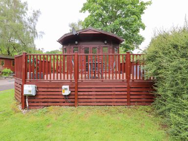 A wooden cabin with a deck and outdoor furniture surrounded by grass and trees at 10 Thirlmere White Cross Bay near Troutbeck Bridge