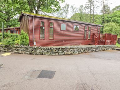 A red wooden cabin with windows and a small porch surrounded by trees at 10 Thirlmere White Cross Bay near Troutbeck Bridge