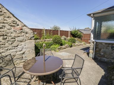 An outdoor patio with a round table and four chairs next to stone walls and a garden at Ty Uchaf in Dyffryn Ardudwy