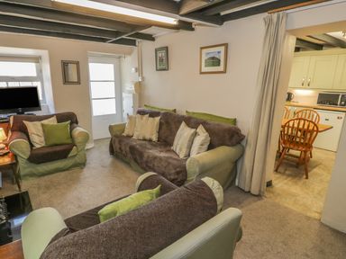 A living room with sofas and cushions a television and an adjoining kitchen with a dining table and chairs at Ty Uchaf in Dyffryn Ardudwy