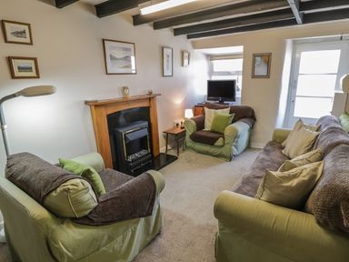 A living room with a fireplace two armchairs a sofa a television and framed pictures on the walls at Ty Uchaf in Dyffryn Ardudwy