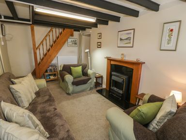 A living room with sofa armchairs fireplace and wooden staircase at Ty Uchaf in Dyffryn Ardudwy