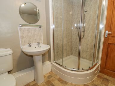 A bathroom with a toilet sink round mirror glass shower enclosure and wooden door at Ty Uchaf in Dyffryn Ardudwy