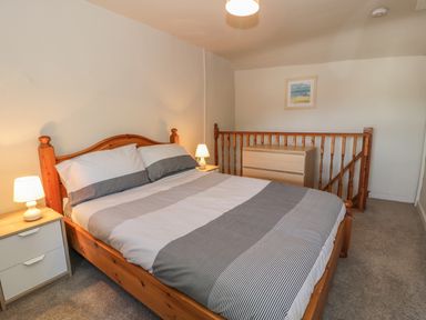 A bedroom with a wooden bed a bedside table with a lamp and a chest of drawers at Ty Uchaf in Dyffryn Ardudwy
