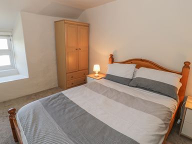 A bedroom with a wooden bed a wooden wardrobe a bedside table with a lamp and a window at Ty Uchaf in Dyffryn Ardudwy