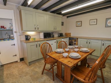 A kitchen with wooden dining table set with plates bowls and glasses and green cabinets at Ty Uchaf in Dyffryn Ardudwy