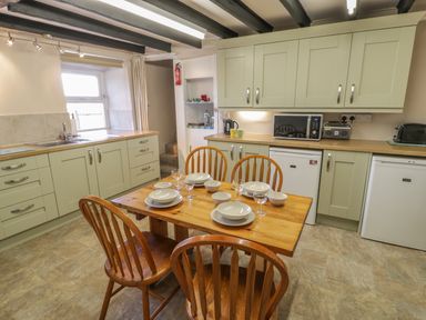 A kitchen with wooden table and chairs set with plates and glasses alongside green cabinets and appliances at Ty Uchaf in Dyffryn Ardudwy