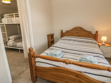 A bedroom with a wooden double bed striped bedding and towels with a nook containing bunk beds at Ty Uchaf in Dyffryn Ardudwy
