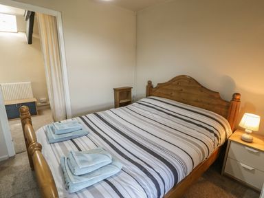 A bedroom with a wooden bed with striped bedding two sets of towels on the bed a bedside table with a lamp and a small wooden shelf unit at Ty Uchaf in Dyffryn Ardudwy