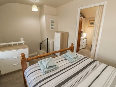 A bedroom with a wooden bed with striped bedding and folded towels a chest of drawers and a small table visible through a doorway at Ty Uchaf in Dyffryn Ardudwy