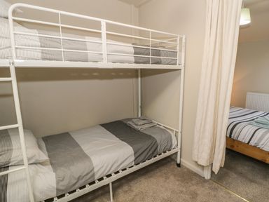 A bedroom with a white metal bunk bed with striped bedding and a bed with striped bedding separated by a curtain at Ty Uchaf in Dyffryn Ardudwy