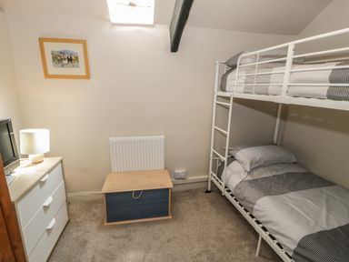 A small bedroom with a bunk bed a chest of drawers with a lamp and a small chest at Ty Uchaf in Dyffryn Ardudwy
