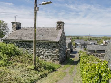 A stone house with a slate roof and chimneys next to a narrow grass path with hedges and a wooden utility pole at Ty Uchaf in Dyffryn Ardudwy