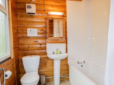 A bathroom with a toilet sink mirror bathtub and wooden wall paneling at Eagle Lodge in Strathpeffer