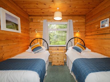 A wooden bedroom with two single beds with blue blankets and multicolored pillows at Eagle Lodge in Strathpeffer