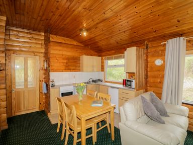 A kitchen and dining area with wooden table and chairs a white leather sofa and wood panel walls at Eagle Lodge in Strathpeffer