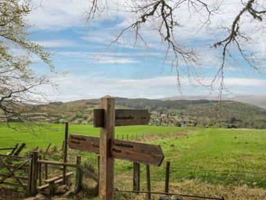 A countryside path with wooden signposts and a gate overlooking fields and hills at Eagle Lodge in Strathpeffer