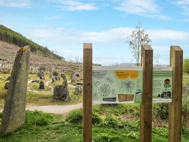 An outdoor stone circle with informational signs and a forested hillside in the background at Eagle Lodge in Strathpeffer