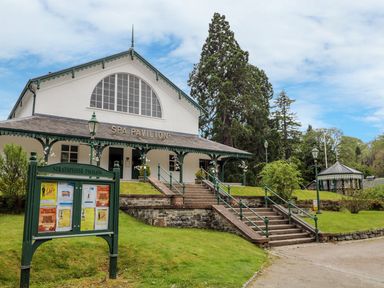 A pavilion building with a sign reading Spa Pavilion and a notice board on a grassy area at Eagle Lodge in Strathpeffer