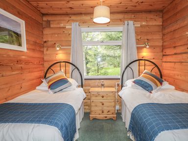 A bedroom with two single beds a wooden nightstand between them and a window with curtains at Otter Lodge in Strathpeffer