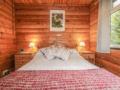 A bedroom with a bed side tables lamps and a window at Otter Lodge in Strathpeffer