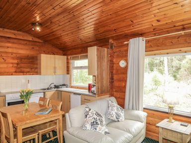 A kitchen and dining area with wooden table and chairs and a small sofa near a window at Otter Lodge in Strathpeffer