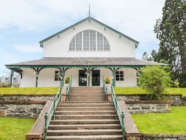 An entrance with stairs leading up to a building labeled Spa Pavilion with green railings and white walls at Otter Lodge in Strathpeffer
