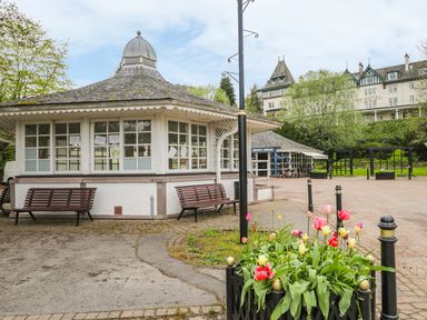 An outdoor area with a white gazebo with benches near colorful flowers and a large hotel building in the background at Otter Lodge in Strathpeffer