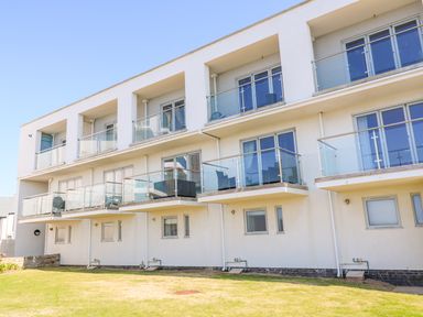 A three story apartment building with glass balconies and a grass lawn at Ocean Seven in Newquay