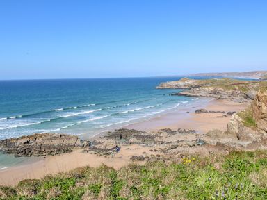 A coastal landscape with sandy beach rocky cliffs and ocean waves at Ocean Seven in Newquay