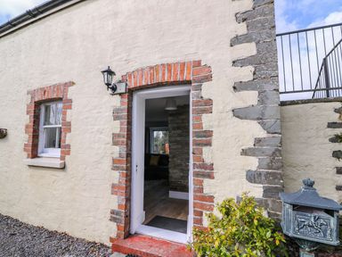 An exterior wall with a door and window framed in red bricks and a black lamp above the door at Bwthyn Y Jacdo in Crymych