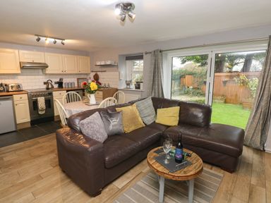 An open plan kitchen and living area with a brown leather sofa and a small round wooden table with wine and glasses at Bwthyn Y Jacdo in Crymych