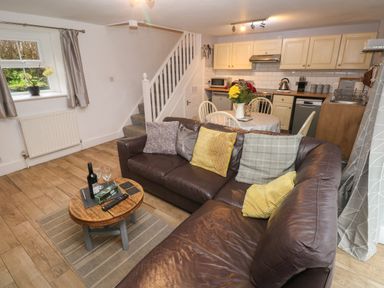 A living area with a brown leather sofa, wooden coffee table, round dining table with chairs, and kitchen with cream cabinets at Bwthyn Y Jacdo in Crymych