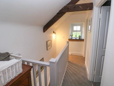 A hallway with a wooden chest and a basket on top a white railing and a window with small plants on the sill at Bwthyn Y Jacdo in Crymych