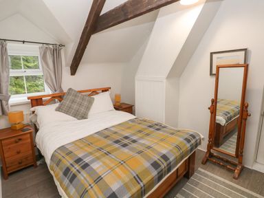 A bedroom with a wooden double bed with a patterned blanket two bedside tables with lamps a full length mirror and a window with curtains at Bwthyn Y Jacdo in Crymych