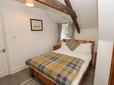 A bedroom with a wooden bed table lamp curtains and a framed painting at Bwthyn Y Jacdo in Crymych