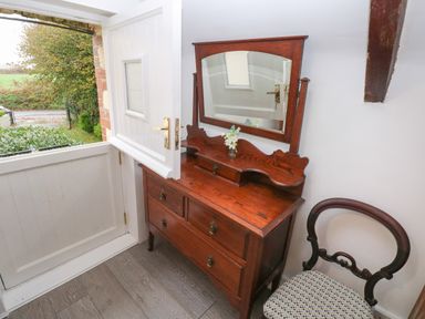 An open white half door next to a wooden dresser with a mirror and a chair with patterned seat at Bwthyn Y Jacdo in Crymych