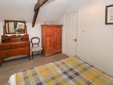 A bedroom with a wooden dresser with mirror a chair a wooden wardrobe and a bed with a patterned blanket at Bwthyn Y Jacdo in Crymych