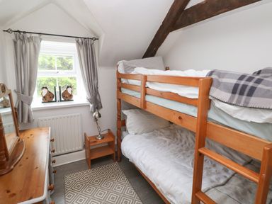 A small bedroom with wooden bunk beds a wooden dresser and a window with curtains at Bwthyn Y Jacdo in Crymych