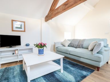 A living room with a blue sofa and a white coffee table with flowers on it at Granary 2 in Madley