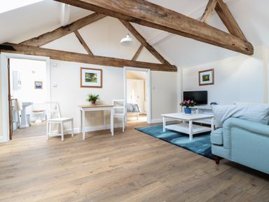 A living room with wooden beams white walls and furniture including a sofa coffee table TV and dining table at Granary 2 in Madley
