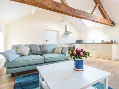A living area with a light blue sofa and cushions next to a white coffee table with flowers and an open kitchen with wooden beams at Granary 2 Madley