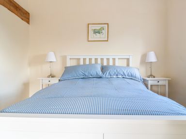A bedroom with a bed with blue striped bedding and two bedside tables with lamps at Granary 2 in Madley