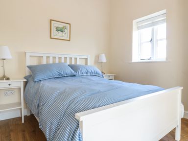 A bedroom with a white bed frame and blue striped bedding two bedside tables with lamps and a window at Granary 2 in Madley