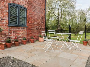 A patio with white metal chairs and table and potted plants near a brick house at Granary 2 in Madley